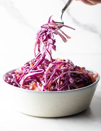 A fork is holding a bite of red cabbage slaw above a bowl of the cabbage slaw recipe.