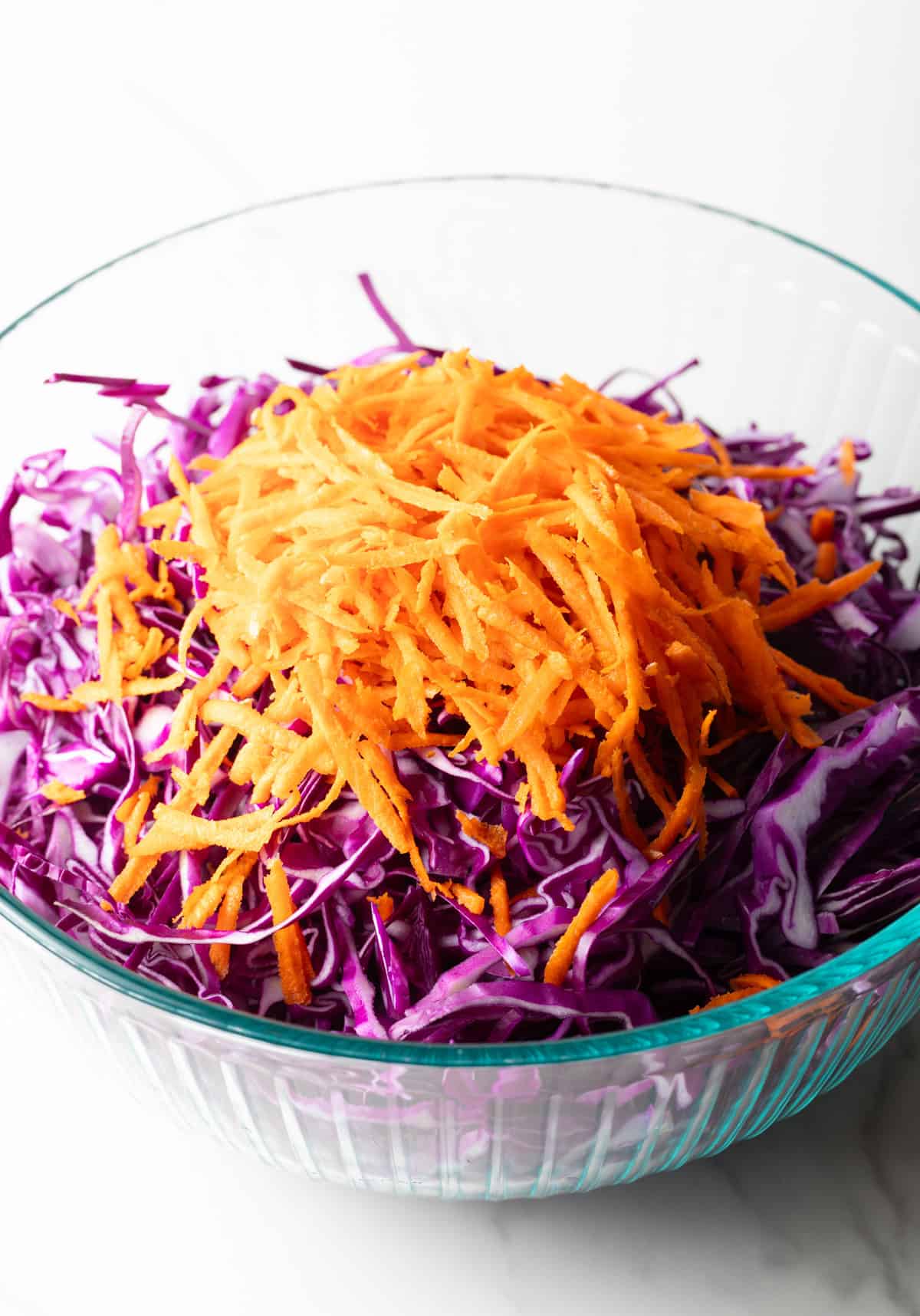 Shredded red cabbage, red onion, and carrots in a glass bowl.