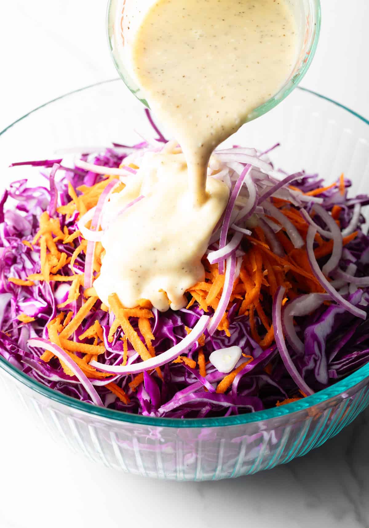 A mayonnaise mixture is being poured over a red cabbage slaw recipe.