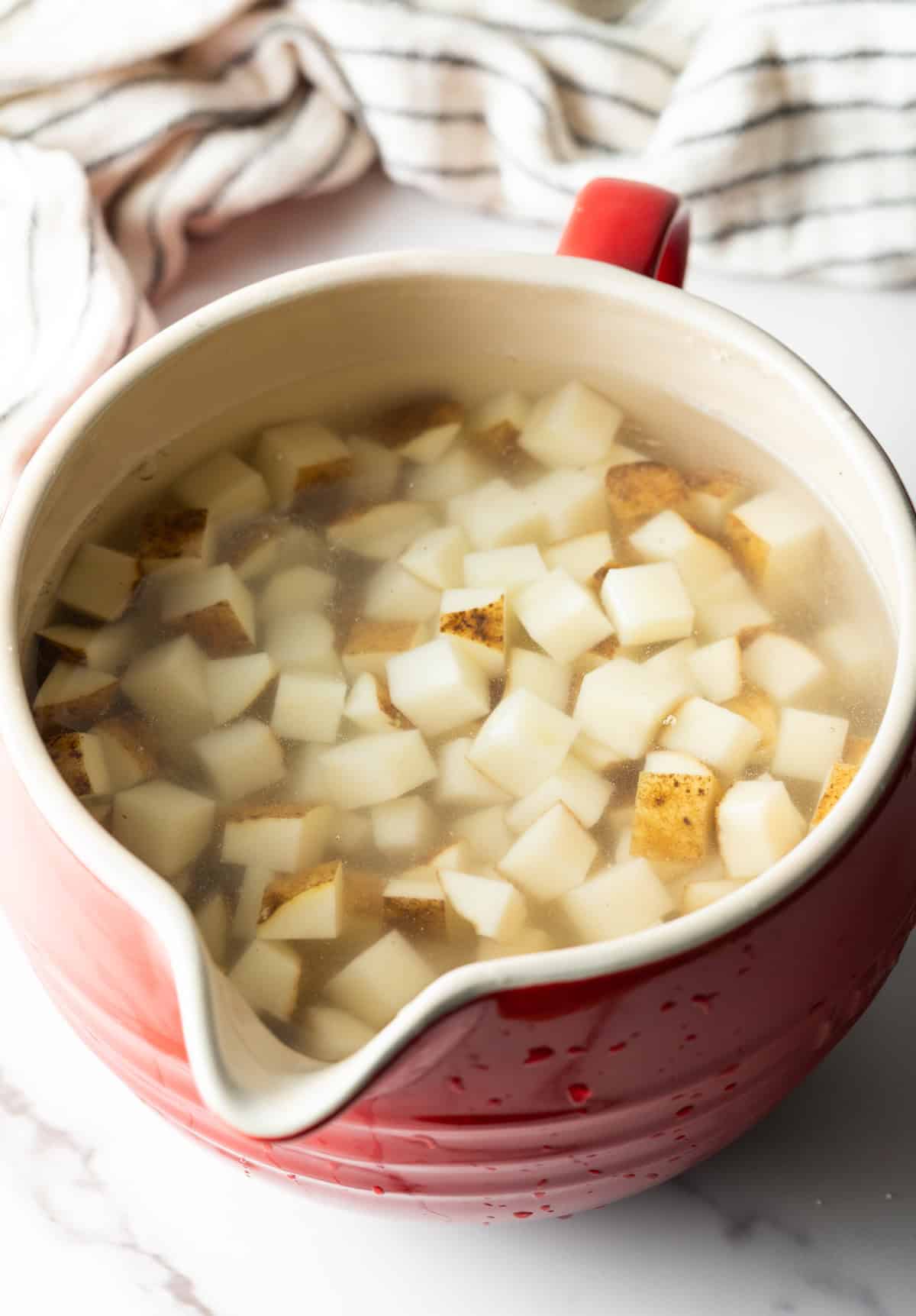 Cubed potatoes sitting in an ice and water bath in a red measuring bowl.