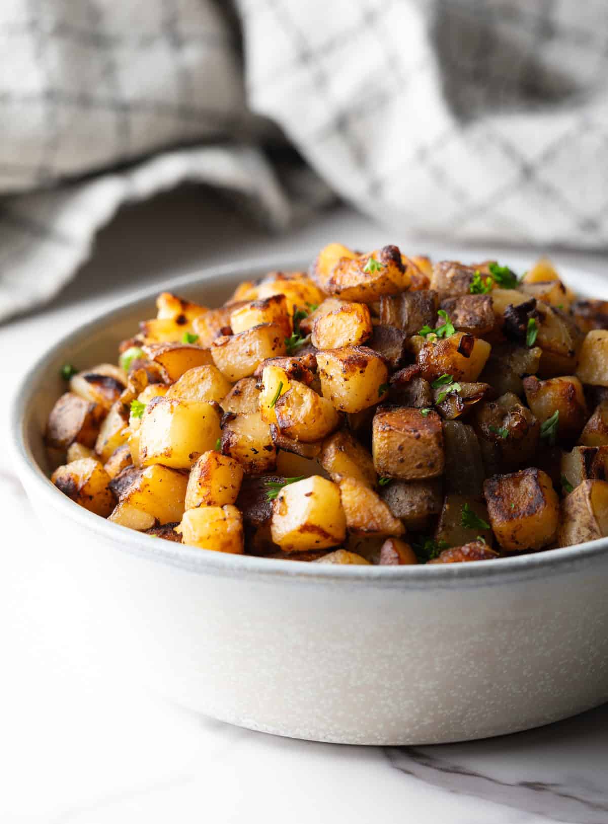 Side view of a white bowl filled with homemade skillet potatoes.
