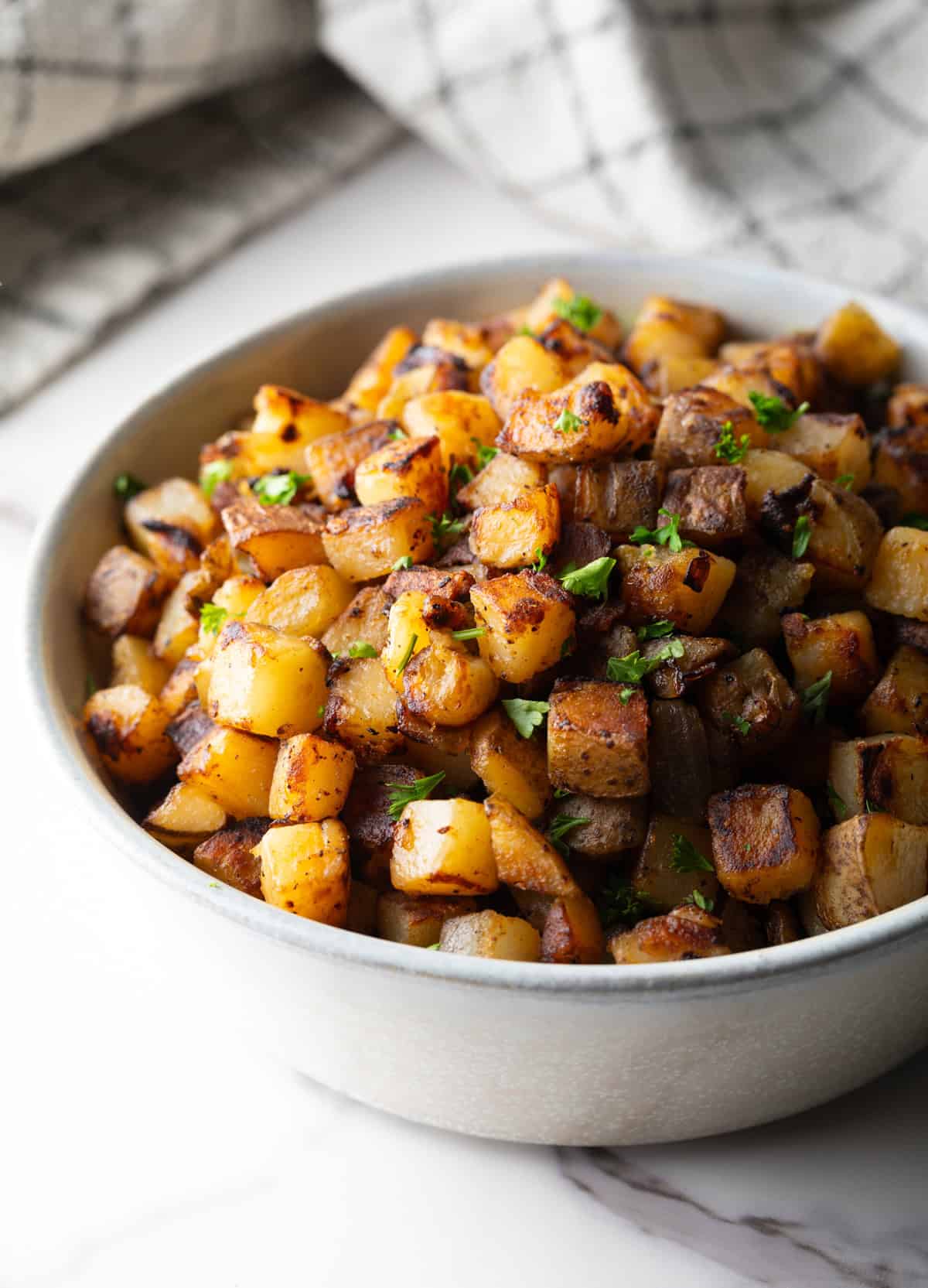 A crispy breakfast home fries recipe topped with fresh parsley, sitting in a white bowl.