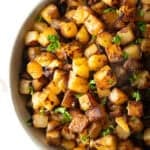 Crispy skillet potatoes garnished with fresh parsley, sitting in a white bowl.