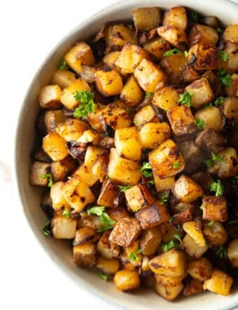 Crispy skillet potatoes garnished with fresh parsley, sitting in a white bowl.