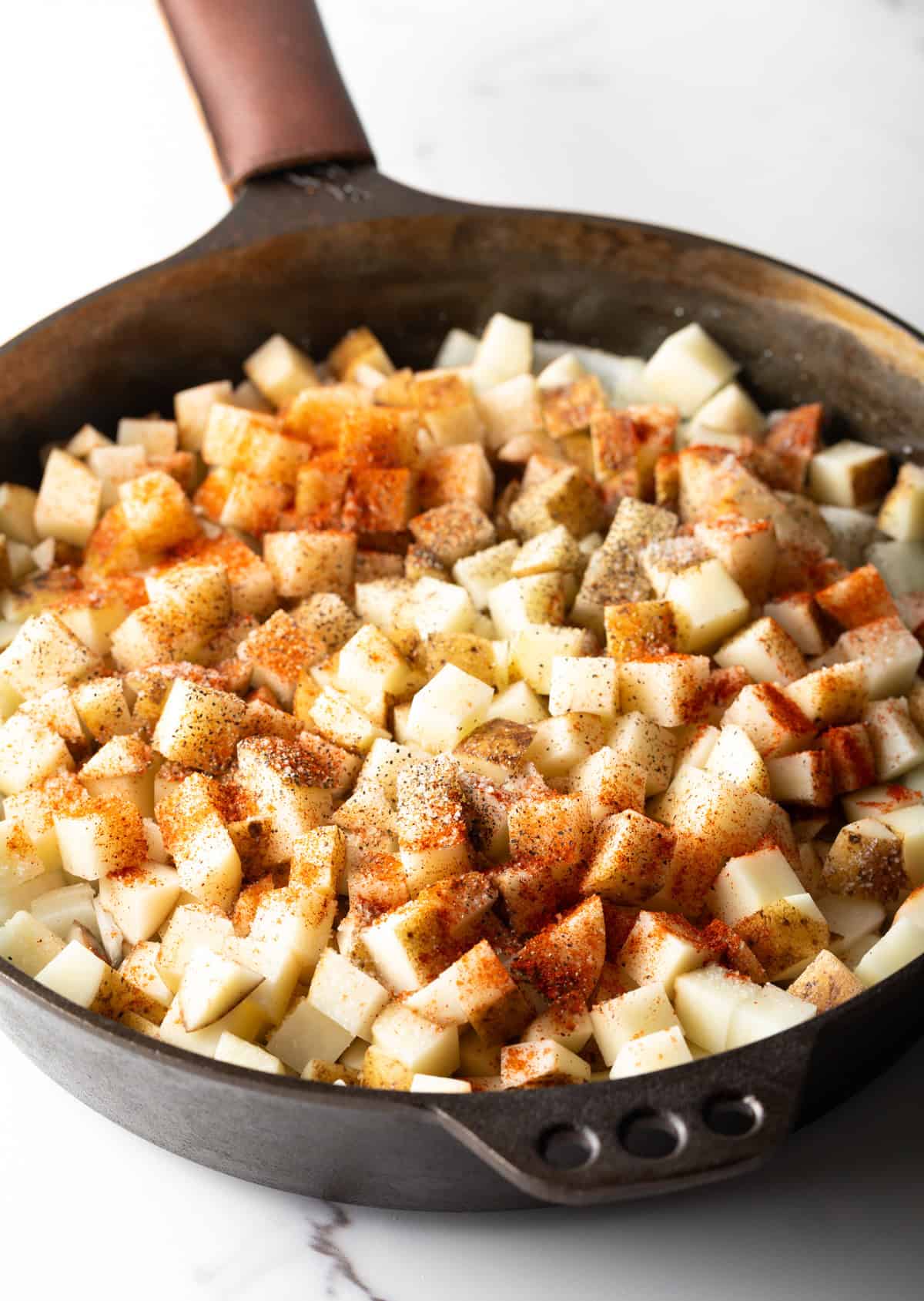 Raw cubed potatoes topped with smoked paprika sitting in a black skillet.