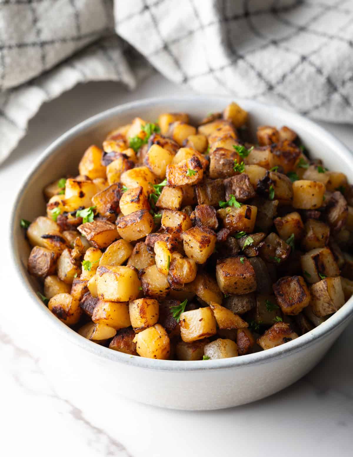 Crispy homefries topped with fresh parsley, sitting in a white bowl ready for serving.