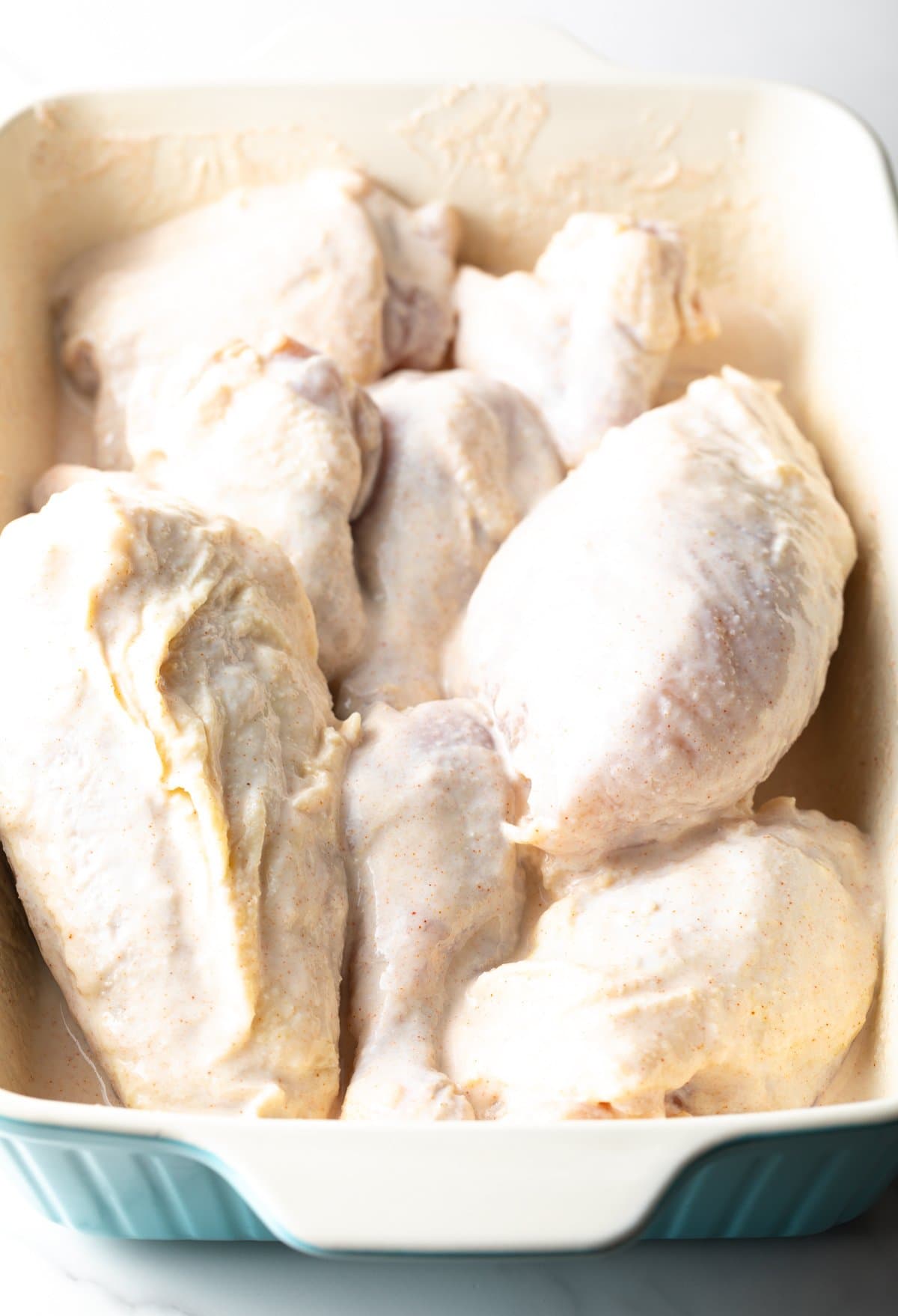 Chicken pieces marinating in a buttermilk mixture sitting in a white baking dish.