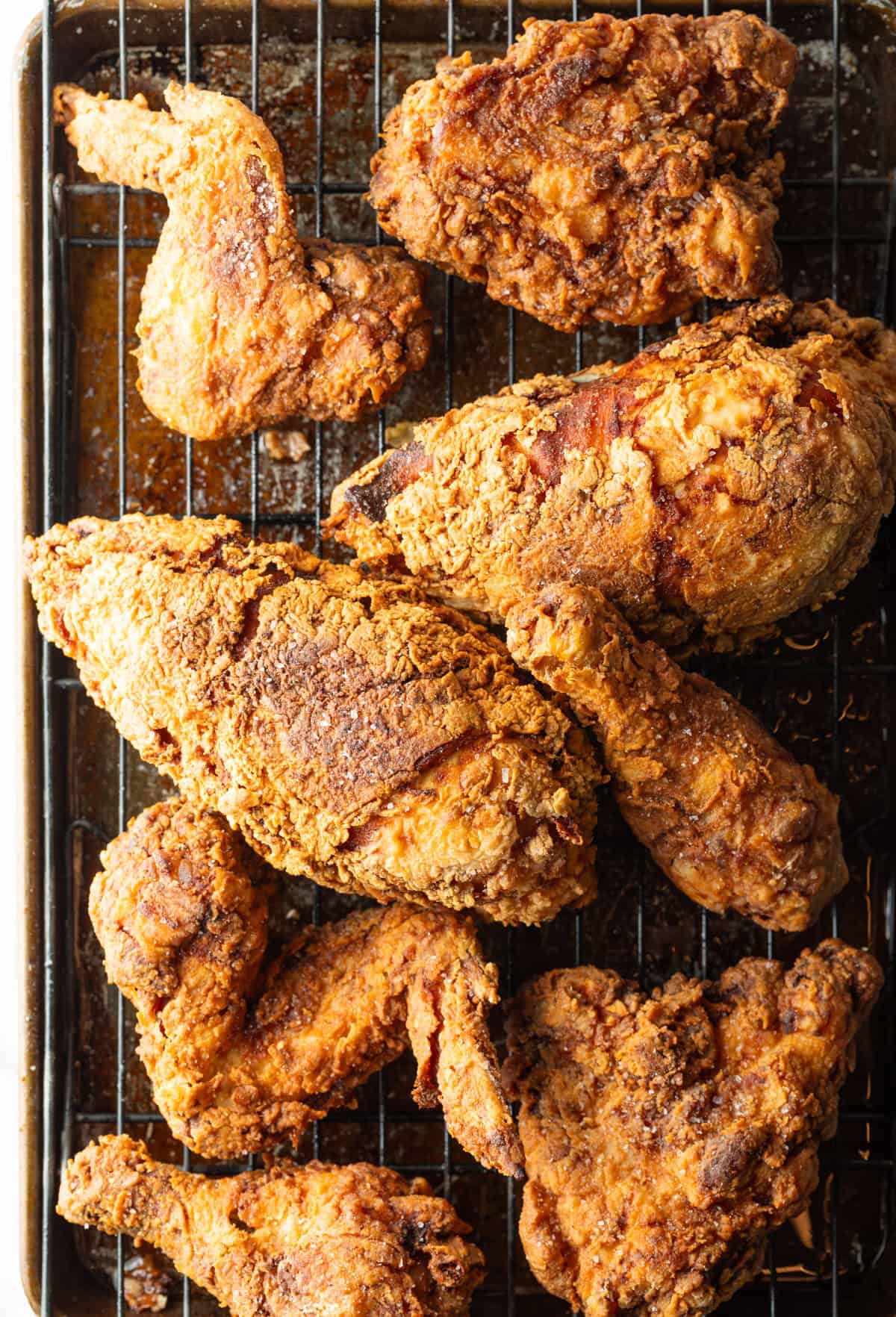 Crispy southern fried chicken cooked in a cast iron skillet, draining on a drying rack.