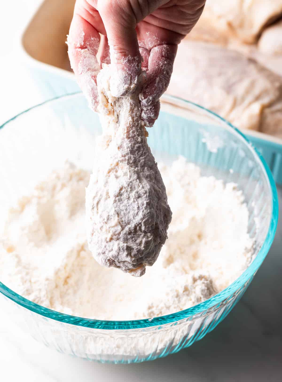 A raw chicken wing is being dredged in a flour mixture for Southern fried chicken.