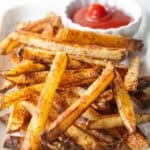 Homemade oven baked French fries sitting on a white plate with a ramekin of ketchup.