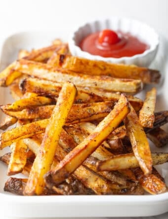 Homemade oven baked French fries sitting on a white plate with a ramekin of ketchup.