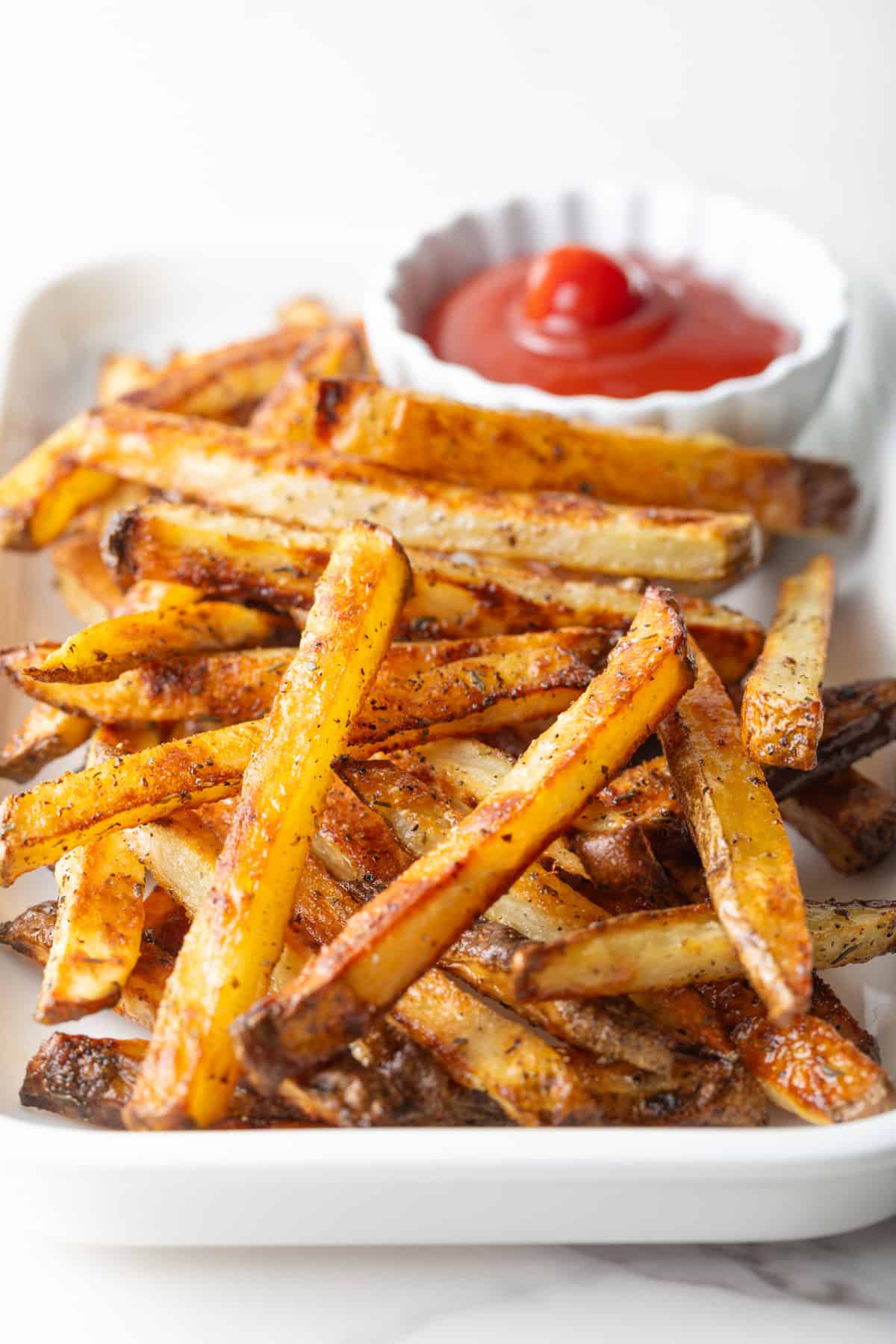 Homemade oven baked French fries sitting on a white plate with a ramekin of ketchup.