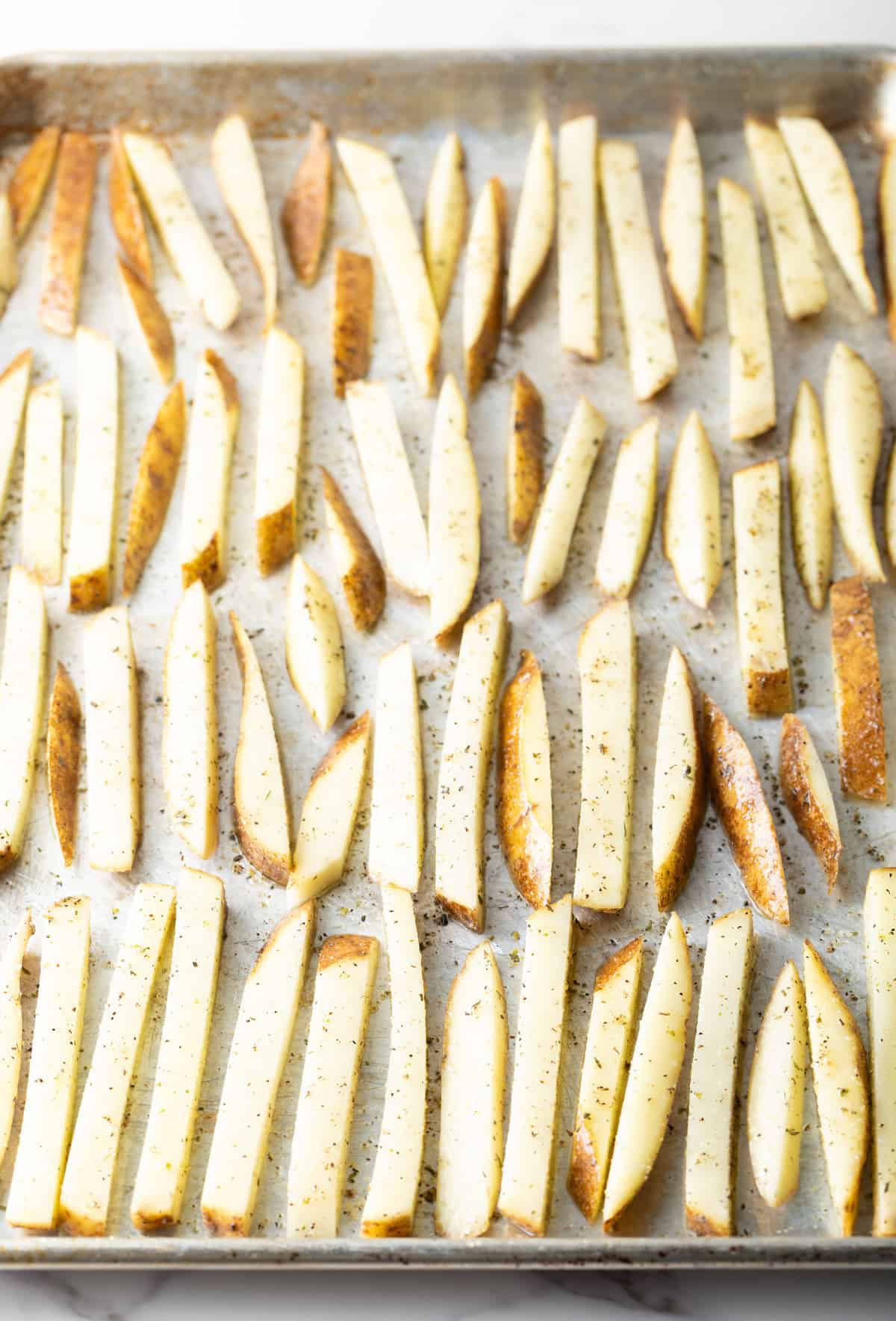 Raw homemade French fries arranged on a baking sheet, ready to be baked in the oven.