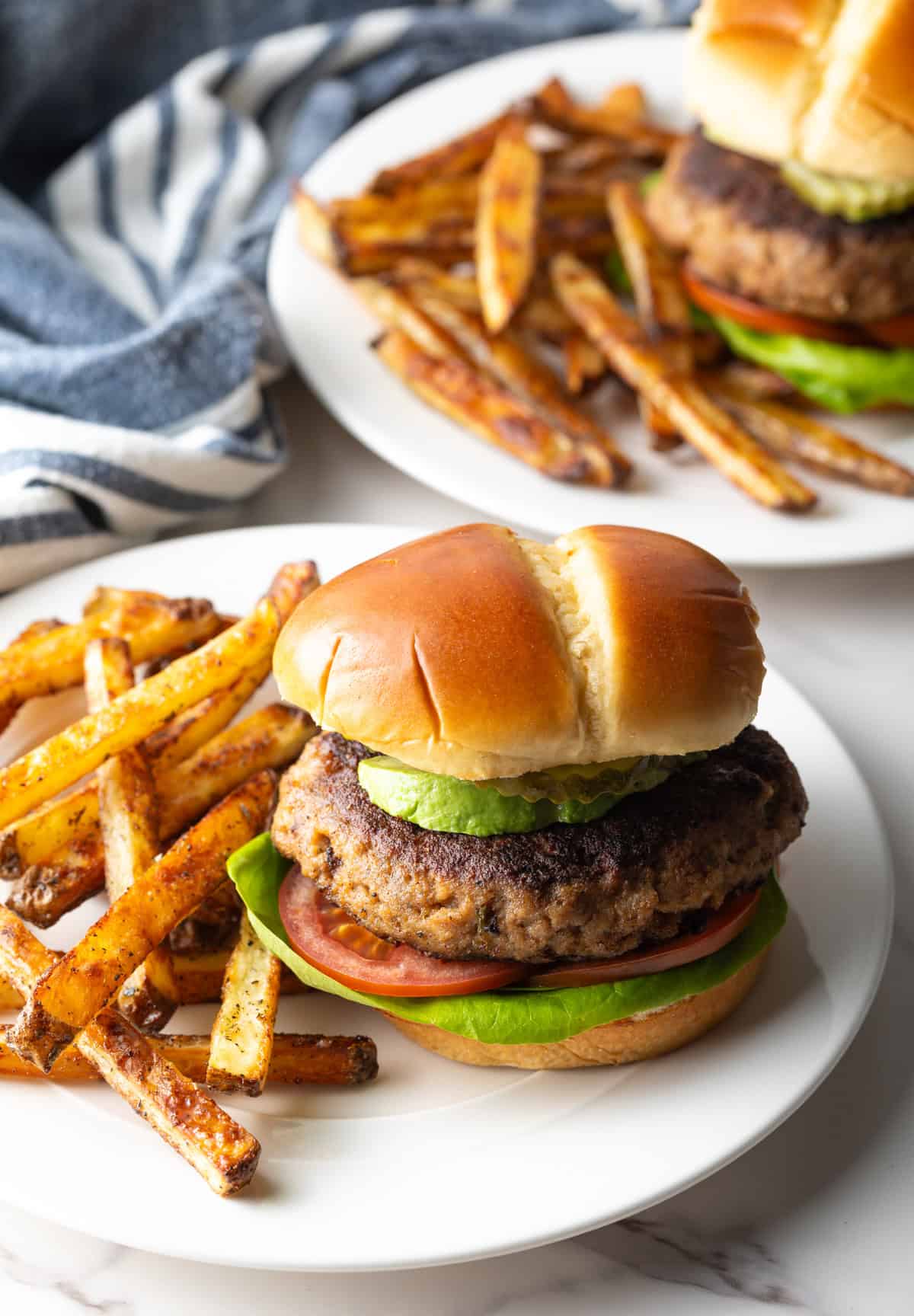 A thick and juicy ground turkey burger sitting on a white plate next to French fries.