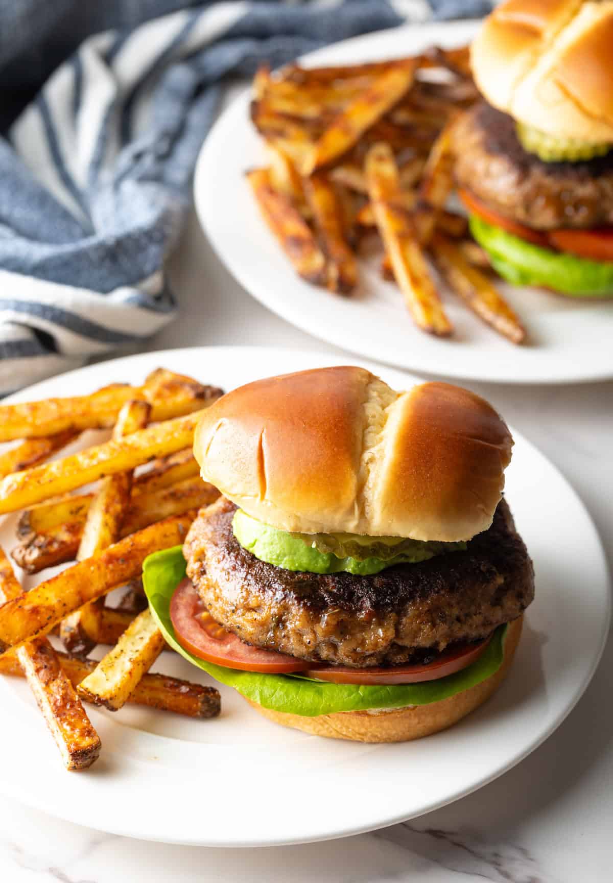 A homemade ground turkey burger inside of a hamburger bun, sitting on a white plate with fries.