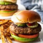 A thick and juicy ground turkey burger sitting on a white plate next to French fries.