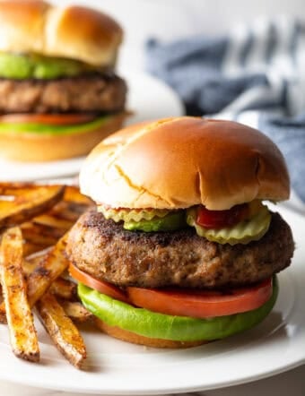 A thick and juicy ground turkey burger sitting on a white plate next to French fries.