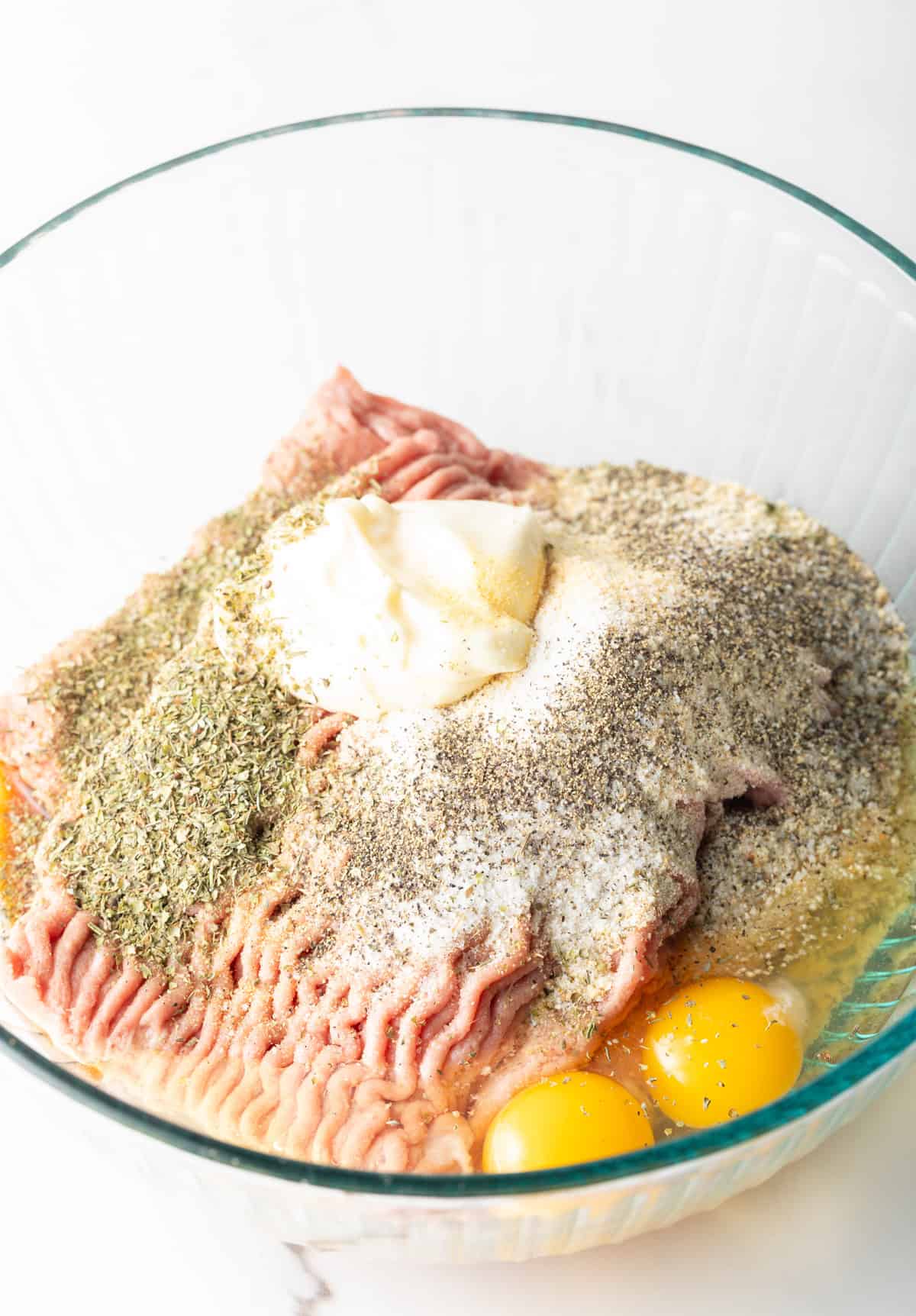 A glass bowl filled with ground turkey, eggs, and seasonings for a turkey burger recipe.
