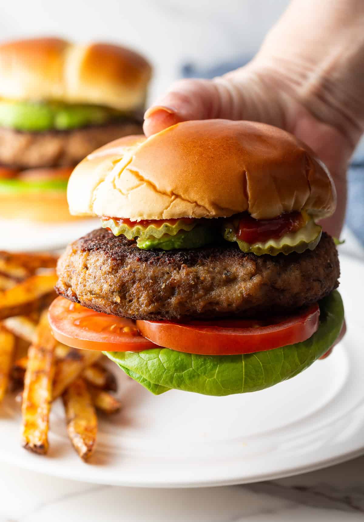 A hand holding a thick ground turkey burger with pickles, lettuce, and tomato.