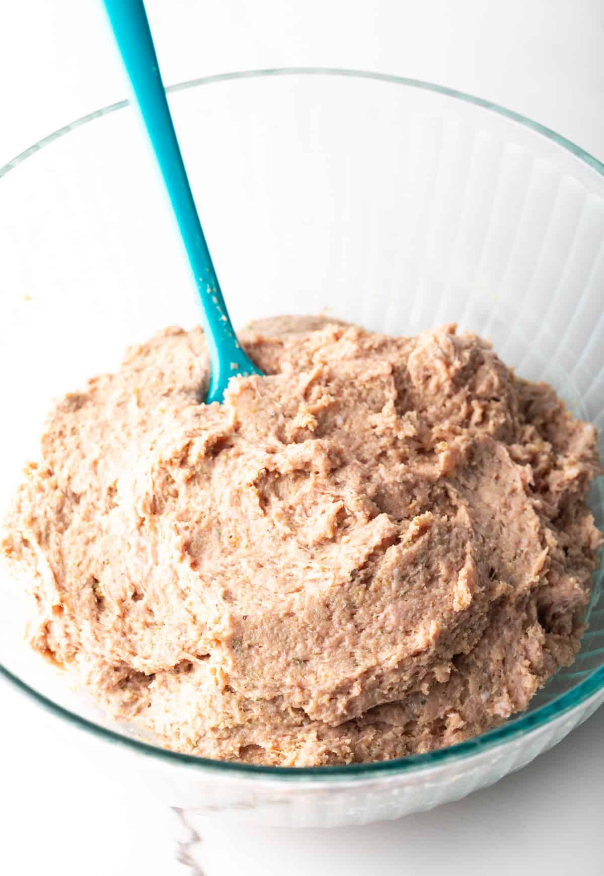 A ground turkey burger mixture in a glass bowl with a blue spatula.