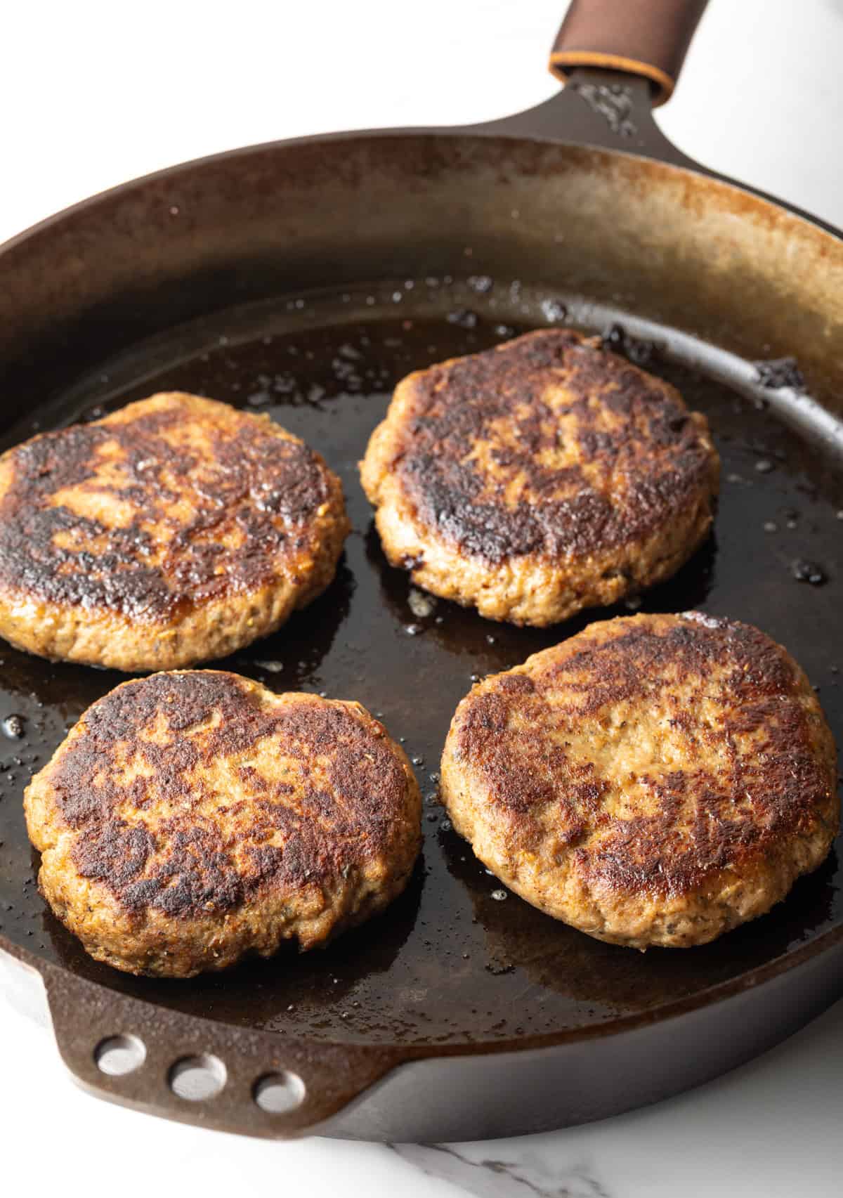 Homemade ground turkey burger patties are being cooked in a black skillet.
