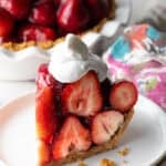 A slice of easy no-bake strawberry pie topped with whipped cream, sitting on a white plate.