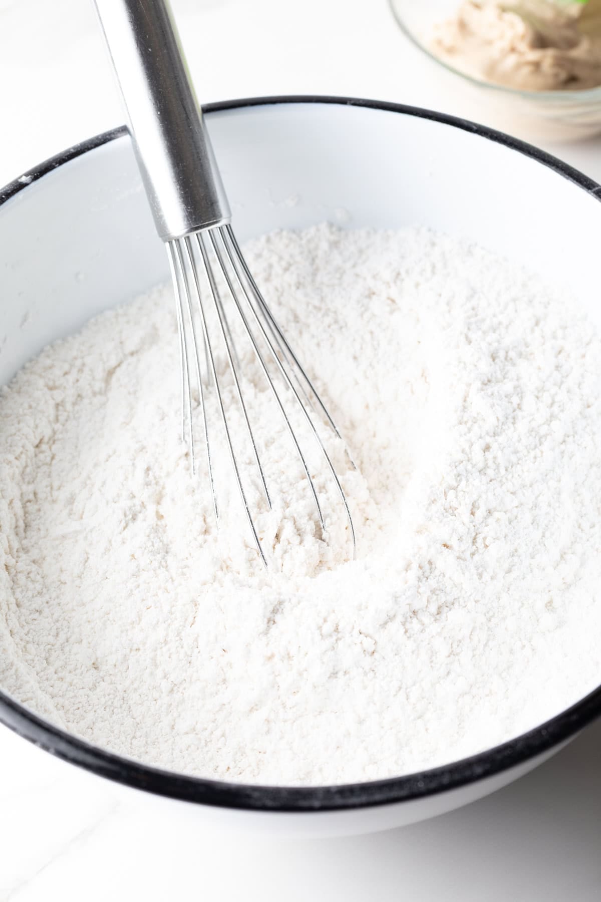 A flour mixture for an angel biscuits recipe is being whisked in a white bowl.