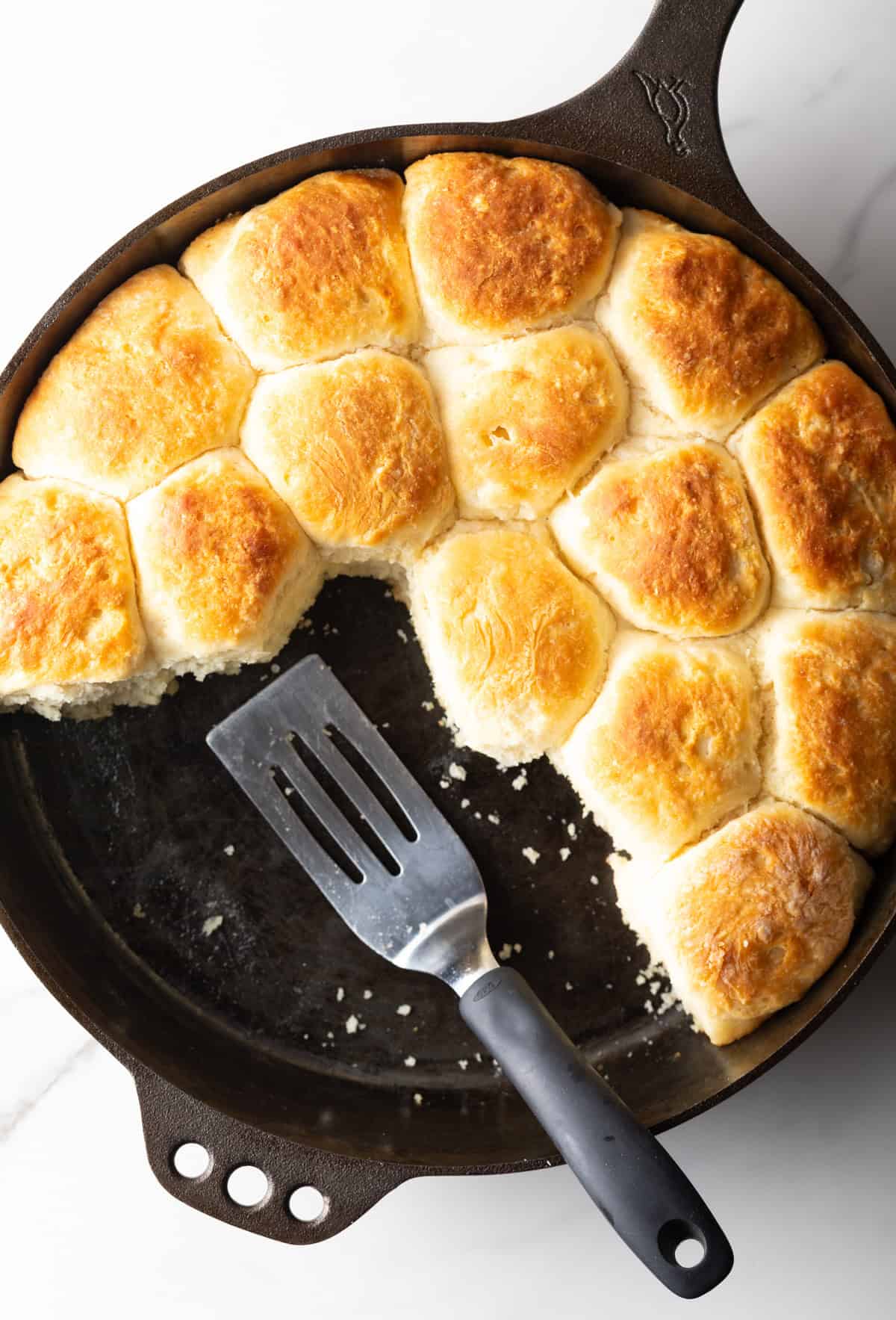An overhead shot of a black skillet filled with an old-fashioned yeast biscuits recipe, with a metal spatula ready for serving.