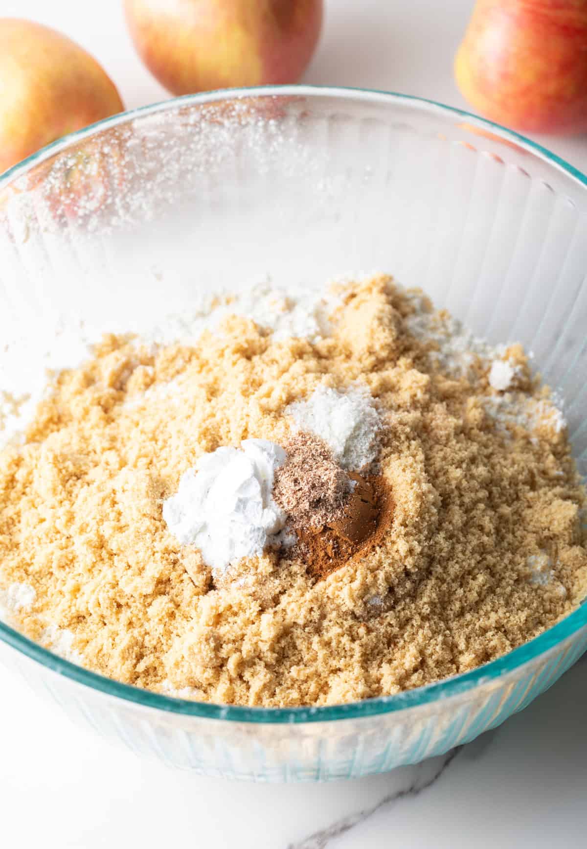 A flour and spice mixture is sitting in a glass bowl for an apple bread recipe.
