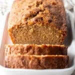 An apple bread recipe on a white dish with two slices cut in front of the loaf.