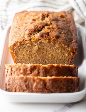 An apple bread recipe on a white dish with two slices cut in front of the loaf.