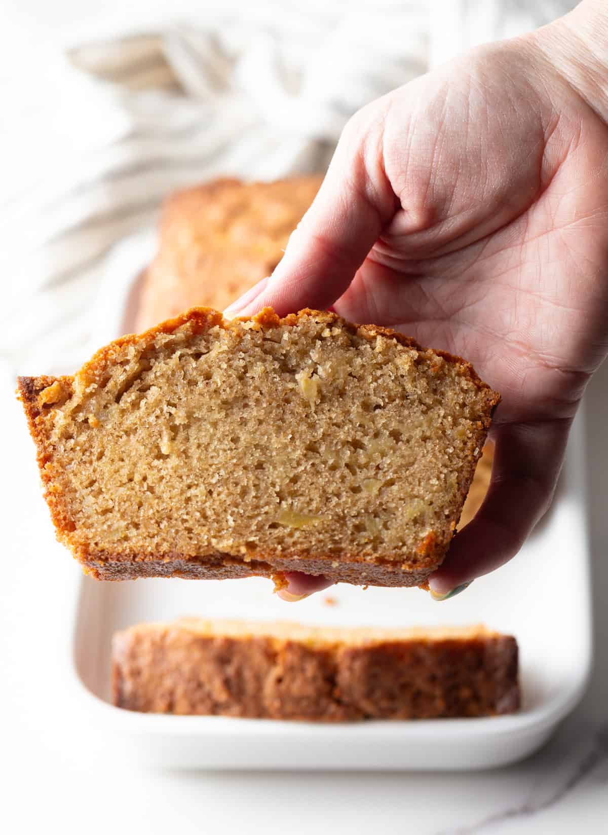 A hand is holding a slice of apple cinnamon bread.