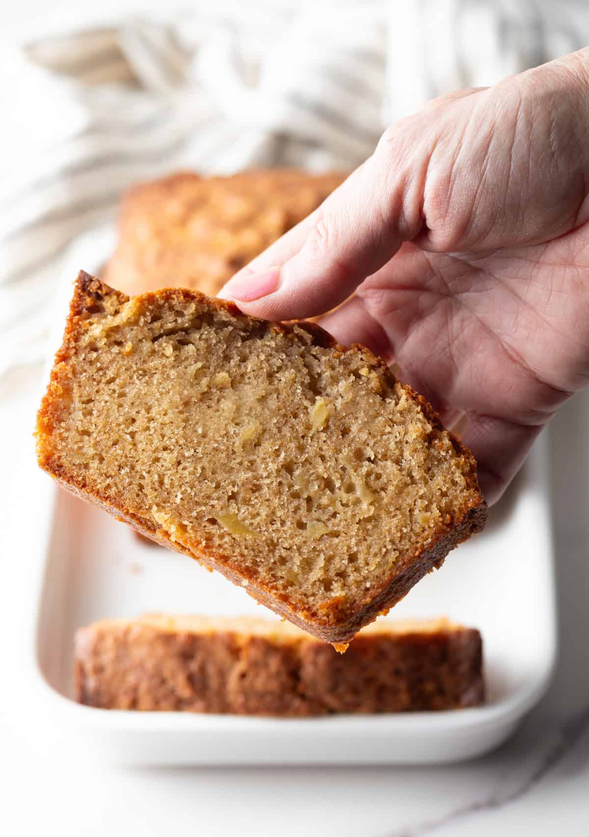 A hand is holding a slice of cinnamon apple bread.