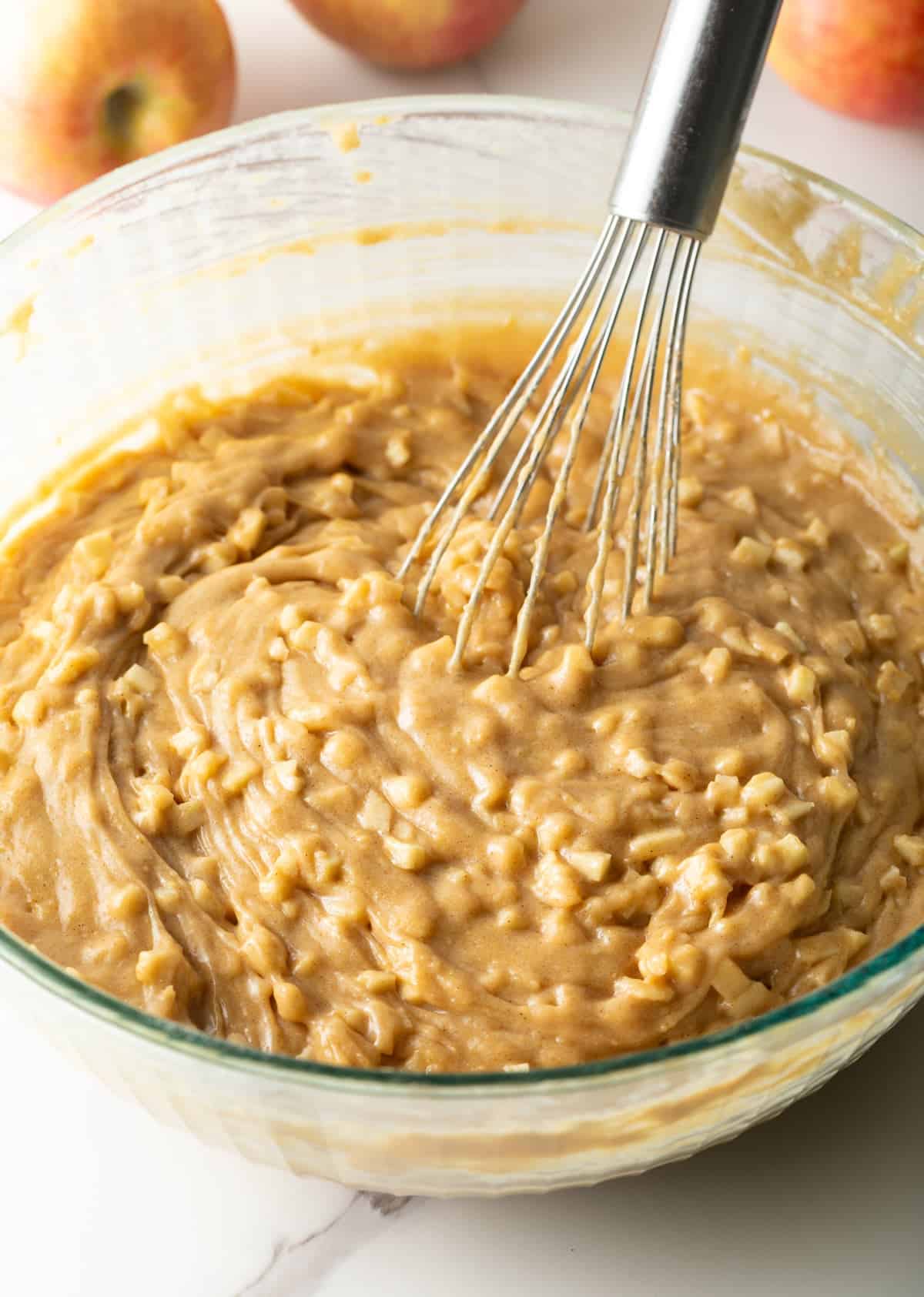 Diced apples have been added to an apple cinnamon bread mixture that is being stirred by a whisk.