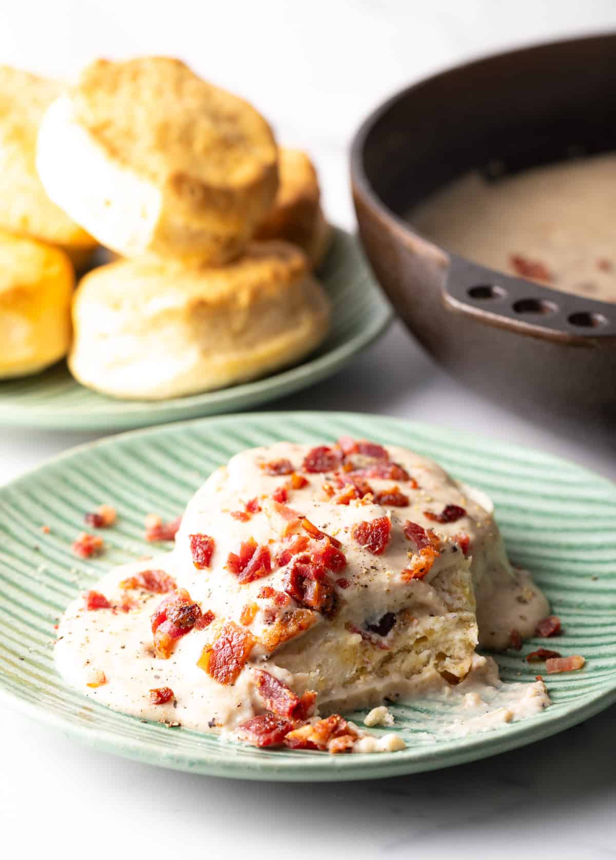 Two biscuits topped with bacon grease gravy, with a bite taken out of one of the biscuits.