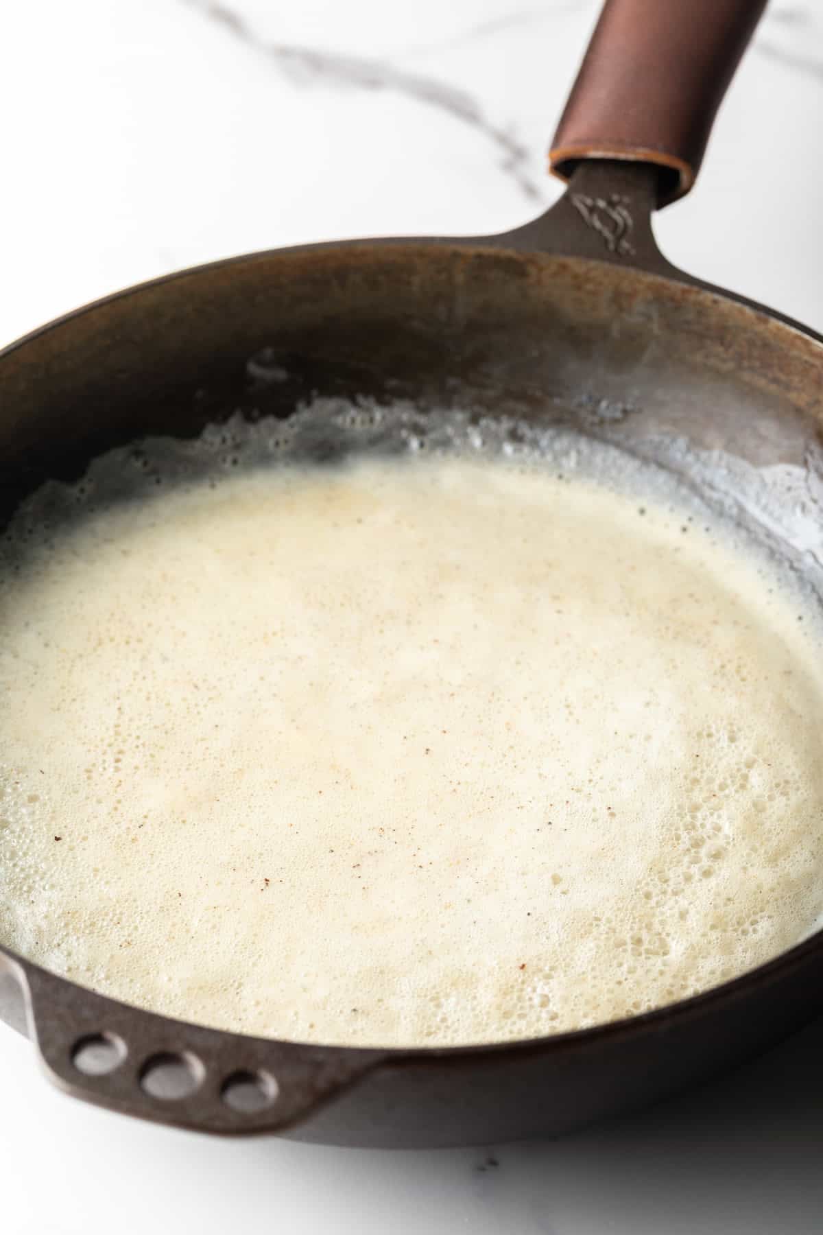 A bacon gravy roux is simmering in a black skillet.