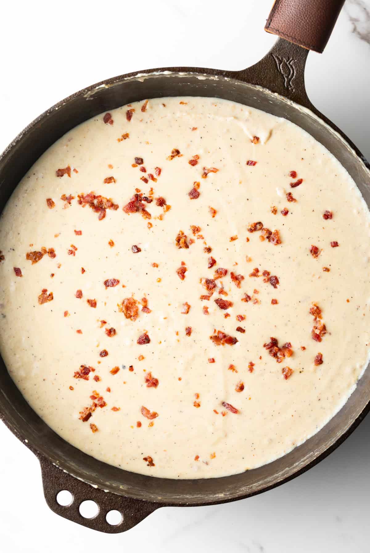 Top down view pieces of chopped bacon in white gravy, in a skillet.