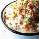 A blue bowl filled with bacon ranch potato salad topped with green onion and chopped bacon.
