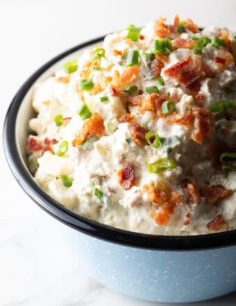 A blue bowl filled with bacon ranch potato salad topped with green onion and chopped bacon.