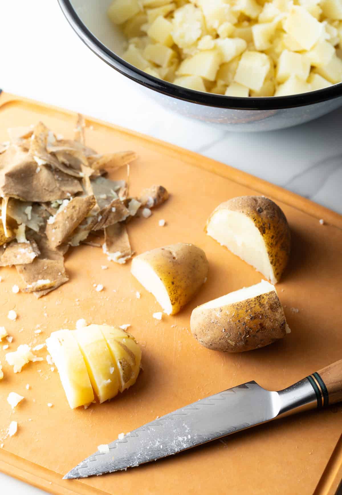 Potatoes are being chopped on a wooden cutting board to prepare for a ranch bacon salad recipe.