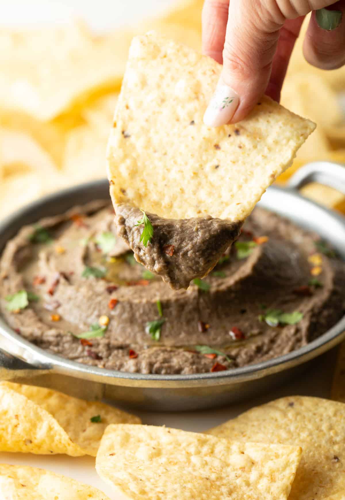 A hand holding a tortilla chip that is being dipped into a homemade black bean dip.