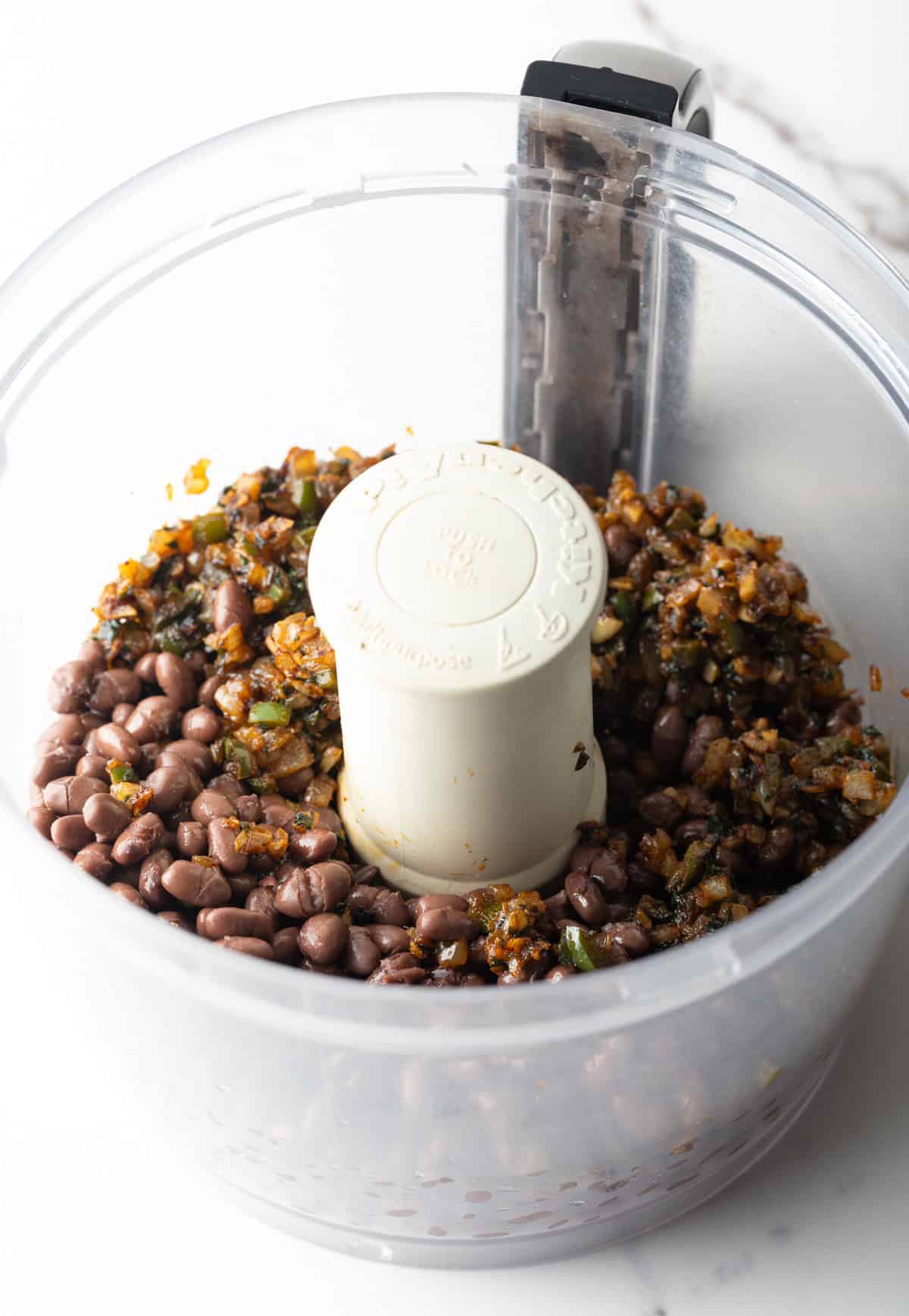 Black beans and sautéed veggies are sitting in a food processor.