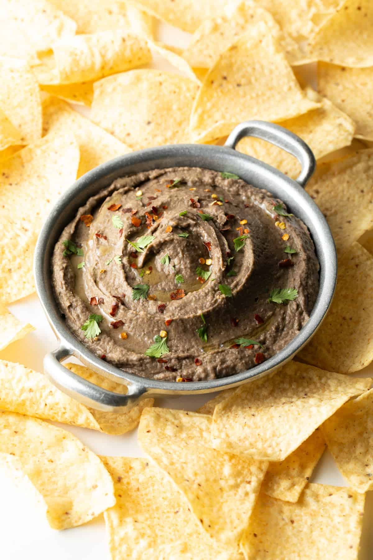 A black bean dip recipe in a metal bowl that is surrounded by tortilla chips.