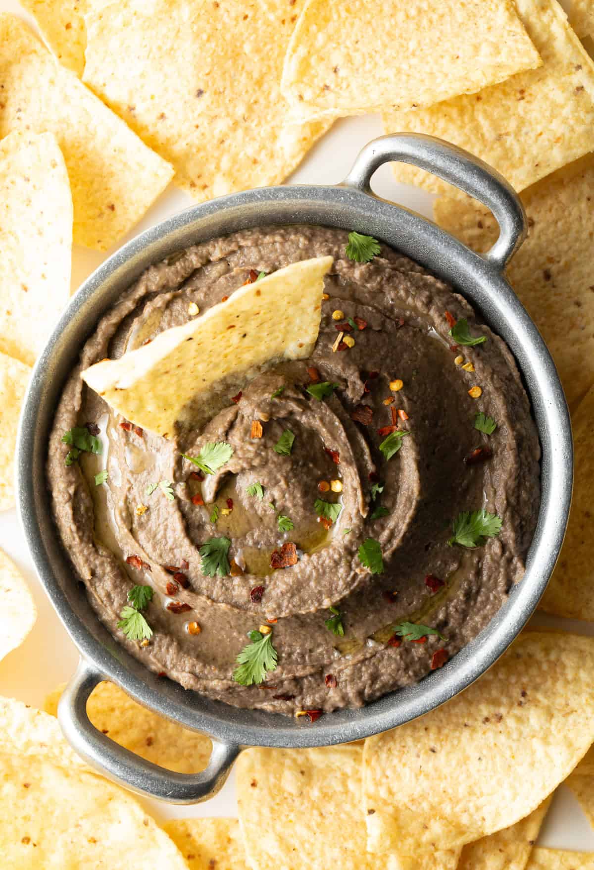 A top-down shot showing a homemade black bean dip recipe with a tortilla chip in the center of the bowl for dipping.