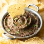 An easy black bean dip in a metal bowl with a tortilla chip sitting in the dip.