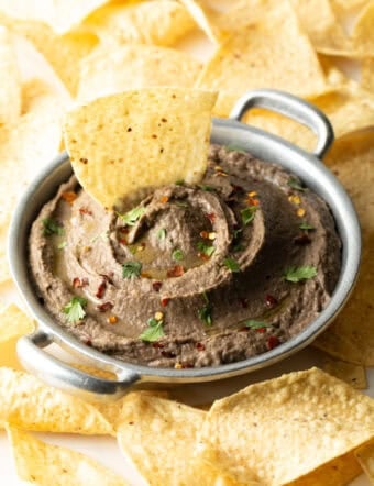 An easy black bean dip in a metal bowl with a tortilla chip sitting in the dip.