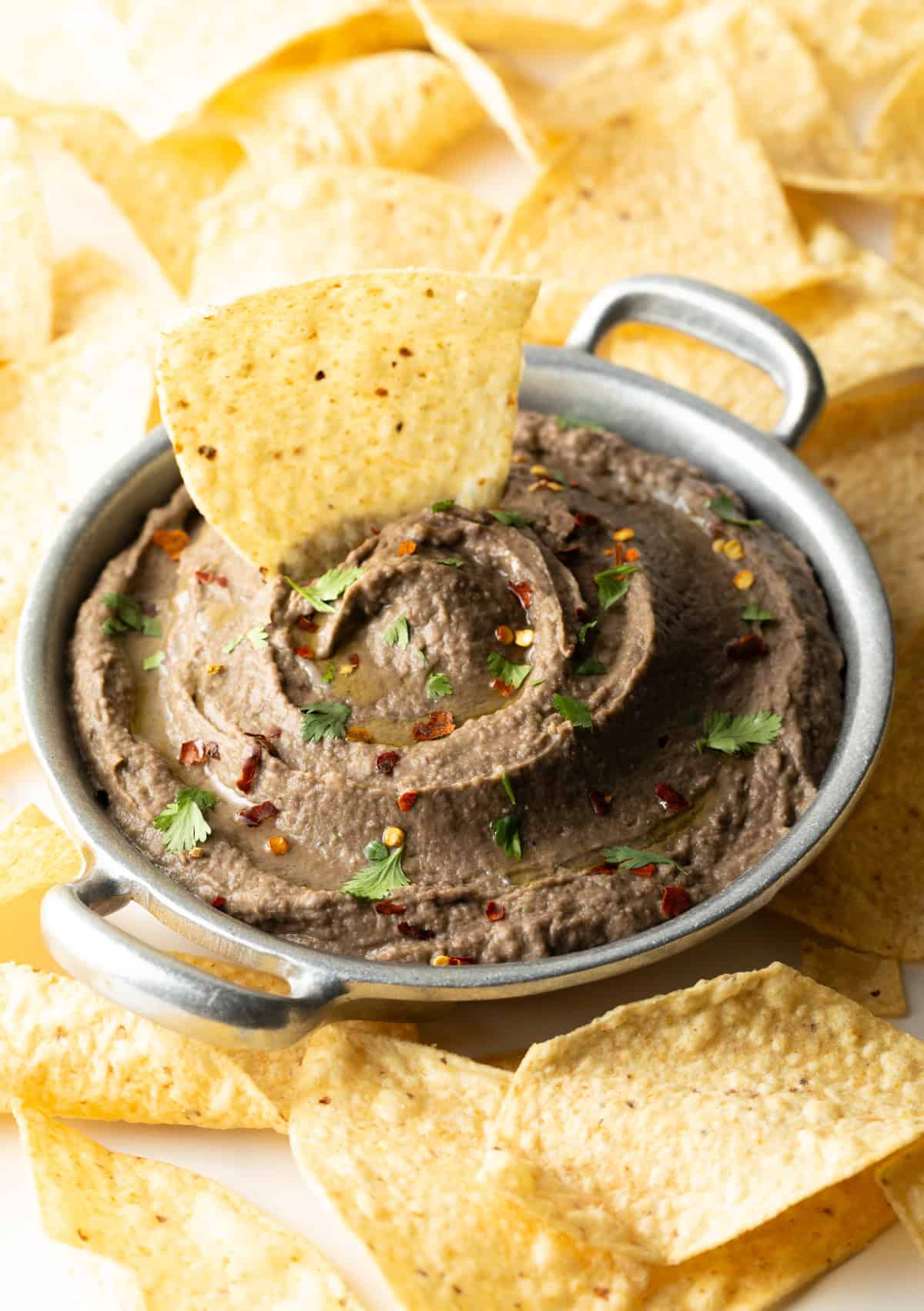 An easy black bean dip in a metal bowl with a tortilla chip sitting in the dip.