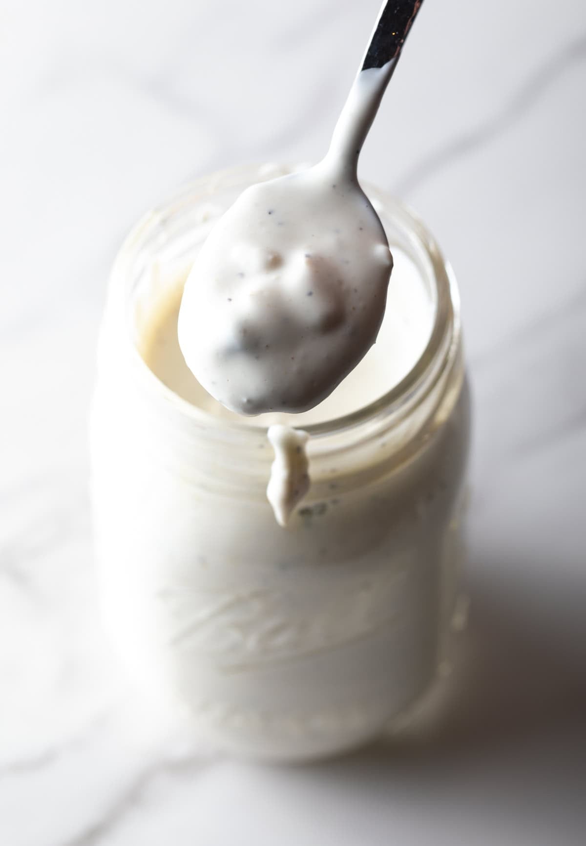 A glass mason jar filled with a blue cheese dressing recipe, with a spoon in the jar.