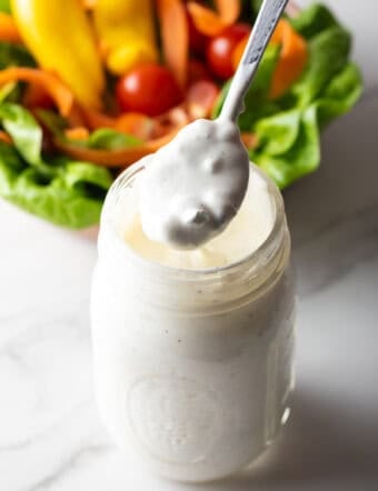 A glass jar filled with homemade blue cheese dressing, with a spoon holding a scoop of the dressing above the jar.