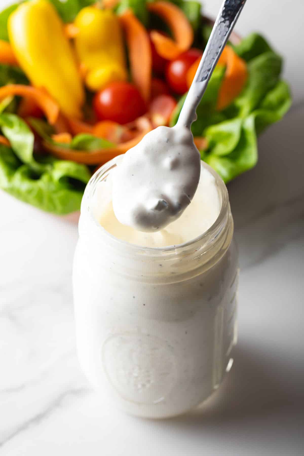 A glass jar filled with homemade blue cheese dressing, with a spoon holding a scoop of the dressing above the jar.